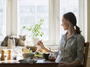 Woman cooking pizza at home. Filling dough with ingredients, while cat relaxing on window